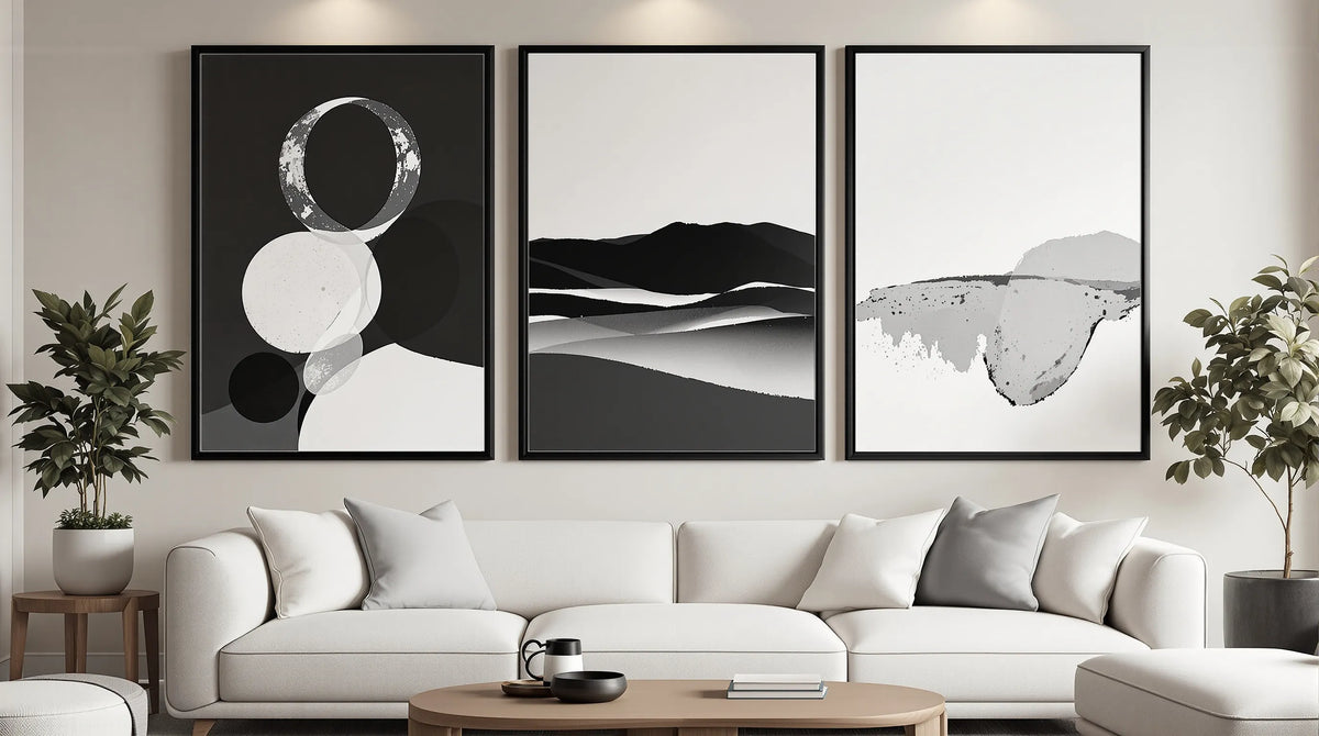 Modern living room gallery wall with three framed black and white art prints — abstract geometric, landscape, and brushstroke styles — above a cream sofa